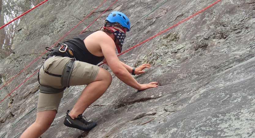 A person wearing safety gear is secured by ropes as they scale a rocky incline. 